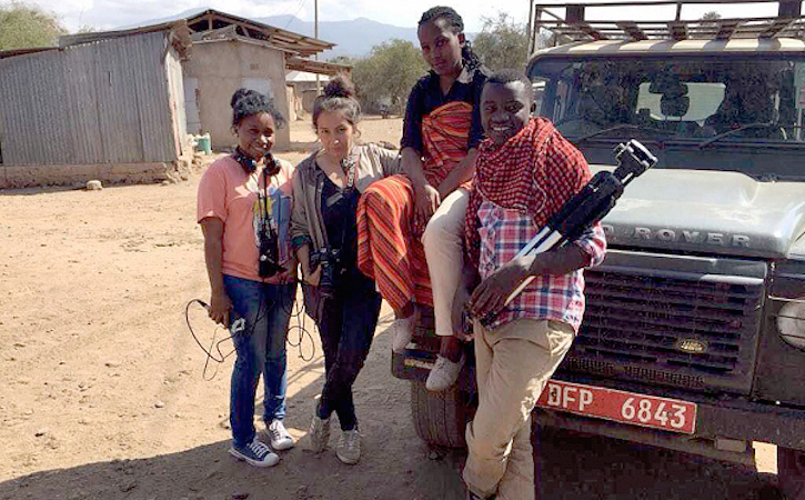 Four students leaning against a jeep