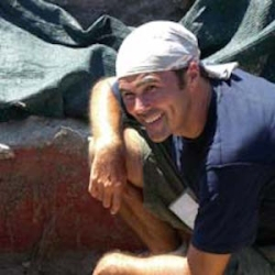 Dr Anderson with light colored bandana on head kneeling at field site in Pompei