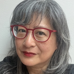 Dr. Wong wearing red glasses and dark top against a white background